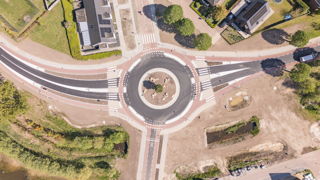 Luchtfoto van een nieuw aangelegde rotonde met fietspaden, rijbanen en verkeersvoorzieningen in een woonomgeving.